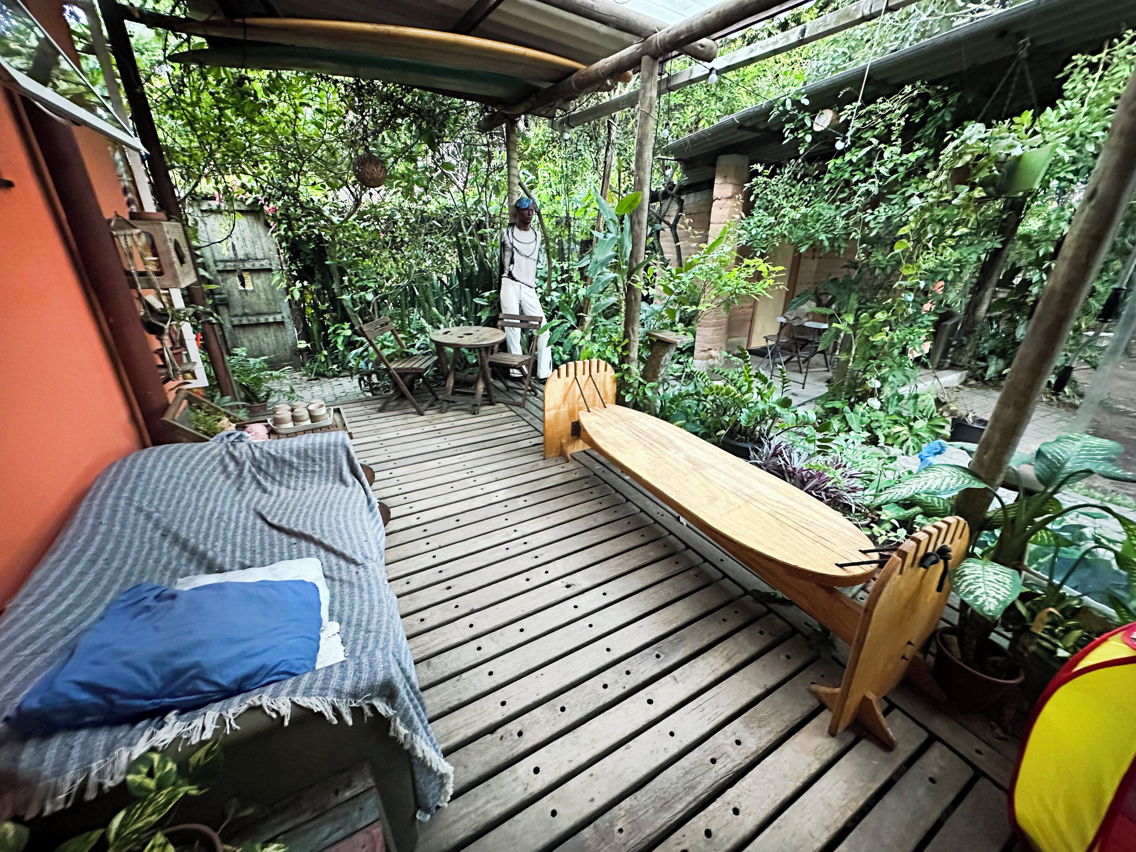A wooden deck with a bench and a table, surrounded by lush greenery and potted plants.