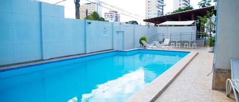 A rectangular swimming pool with clear blue water, surrounded by a tiled deck and a low wall.