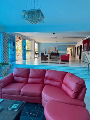 A spacious living area with a red sofa, a piano, and a chandelier. - Hotel Américas (Fortaleza)