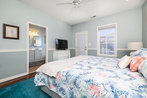 Une chambre à coucher avec un lit, une télévision, un ventilateur de plafond et une fenêtre.