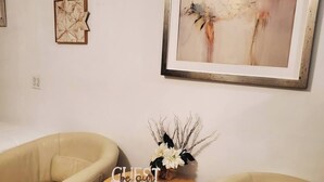 Une pièce comprenant deux canapés en cuir beige, une petite table en bois sur laquelle est posé un vase de fleurs blanches, et un tableau abstrait encadré accroché au mur.