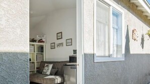 Un intérieur chaleureux avec un canapé, une petite table et un meuble. Les murs sont ornés de tableaux encadrés et il y a une fenêtre avec des volets.