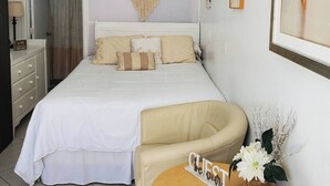 Une chambre à coucher avec un lit, une coiffeuse avec un miroir, un attrape-rêves accroché au mur et un tableau encadré.
