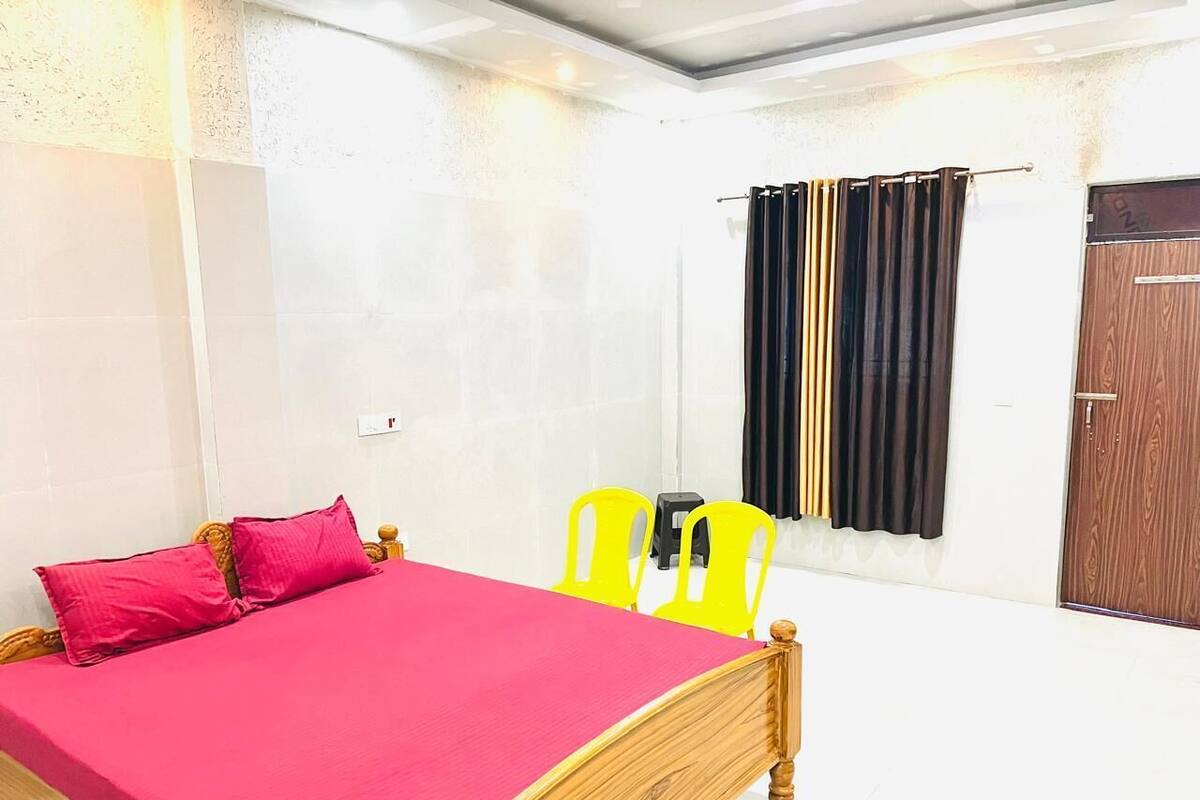 A room with a bed, two chairs, a window with curtains, and a door.
