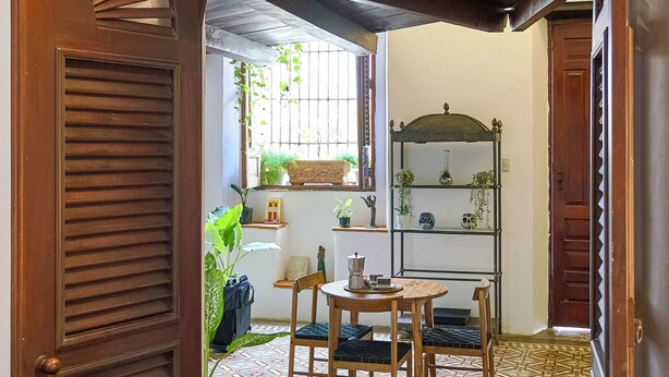 A traditional room with a patterned tile floor, a wooden door, a small table with chairs, and a shelf with plants.