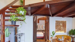 A cozy room with a wooden ceiling, a patterned floor, a bed, a dining table with chairs, and a kitchen area.