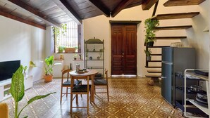 A compact living space with a tiled floor, a wooden ceiling, a dining area with a table and chairs, a television, and a refrigerator.