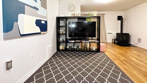 Una sala de estar con alfombra estampada, televisor, estantería, reloj y chimenea.