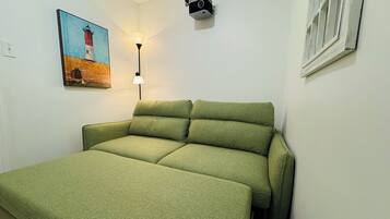 Una stanza con un divano letto verde, un quadro raffigurante un faro, una lampada da scrivania e un proiettore montato a parete.