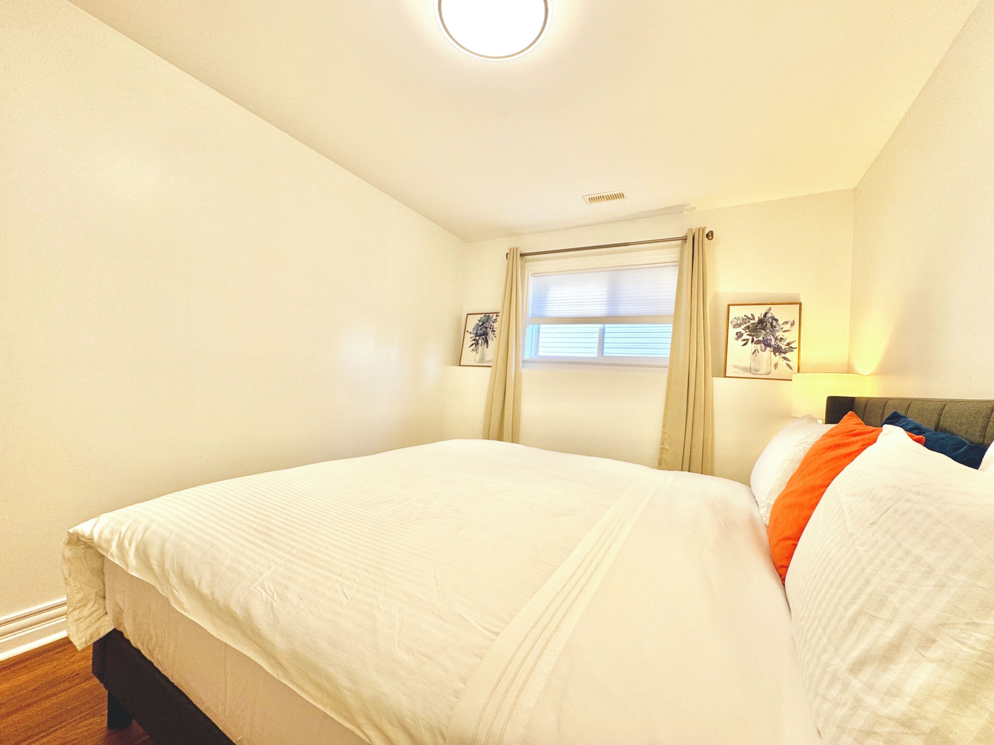 Une chambre à coucher avec un lit, une fenêtre avec des rideaux et deux tableaux accrochés au mur.