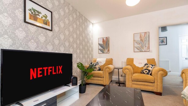A living room with a large flat-screen TV displaying the Netflix logo, two armchairs, a coffee table, and a potted plant. - Spacious 5-Bedroom Family Home with Modern Amenities (Middlesbrough)