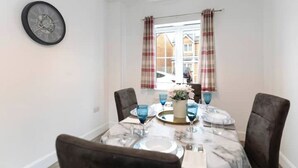 A dining area with a marble table, four chairs, a clock, and a window with curtains. - Spacious 5-Bedroom Family Home with Modern Amenities (Middlesbrough)