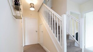 A hallway with a carpeted floor, a white door, and a staircase with white railings. - Spacious 5-Bedroom Family Home with Modern Amenities (Middlesbrough)