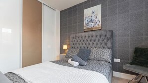 A bedroom with a tufted headboard, patterned bedding, a bedside lamp, and a painting on the wall. - Spacious 5-Bedroom Family Home with Modern Amenities (Middlesbrough)