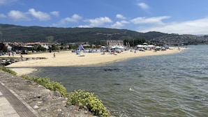 Ein Strand mit Zelten und Menschen, einem gepflasterten Weg und einem Gewässer.