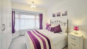 A bedroom with a bed, a bedside table, a lamp, a window with curtains, and framed pictures on the wall. - Host & Stay | Sea Haven (Redcar)