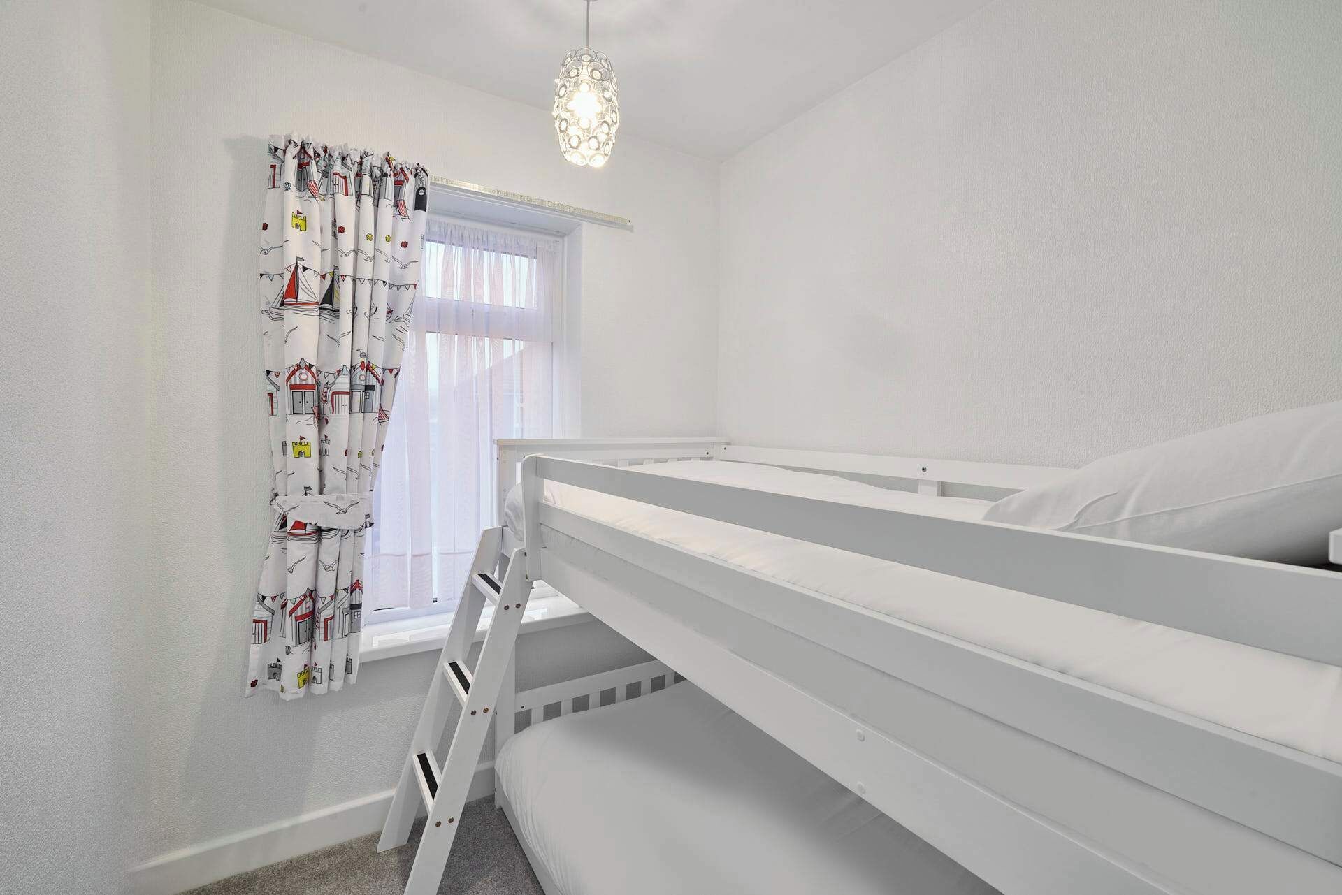 A child's bunk bed room with a ladder, a window with curtains, and a hanging light fixture.