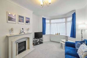 Un salon avec une cheminée, un téléviseur, un canapé bleu et une table basse blanche.