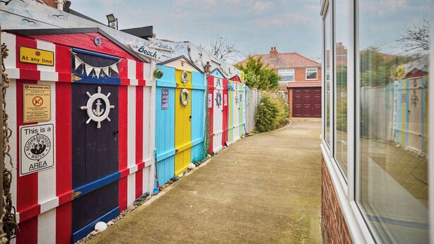 A row of colorful beach huts with a clear path between them. - Host & Stay | Sea Haven (Redcar)
