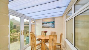 A conservatory with a glass roof, a wooden table with four chairs, and a painting of a beach scene on the wall. - Host & Stay | Sea Haven (Redcar)