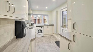 A compact kitchen with a washing machine, microwave, and a coffee maker. - Host & Stay | Sea Haven (Redcar)