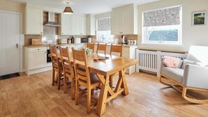 A modern kitchen with white cabinets, a wooden dining table, and a cozy seating area with a grey sofa. - Host & Stay | Audrey's Cottage (Kirk Yetholm)