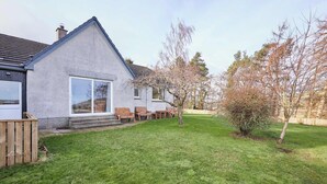 A house with a large glass door, a small patio with wooden furniture, and a well-maintained lawn. - Host & Stay | Audrey's Cottage (Kirk Yetholm)