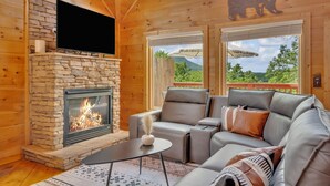 Un interior cálido de cabaña con chimenea de piedra, sofá de cuero y televisión montada en la pared.