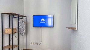 A room with a mounted flat-screen TV displaying a Paramount+ logo, a wooden shelving unit with baskets, and a mirror on the wall. - Central apartment for 4 people with kitchen, WiFi & private parking space (Meißen)