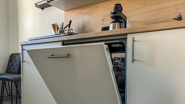 A compact kitchen with a dishwasher, a coffee maker, and a knife holder on the countertop. - Central apartment for 4 people with kitchen, WiFi & private parking space (Meißen)