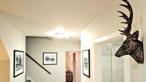 A hallway with framed pictures on the walls, a staircase, and a deer head mounted on the wall. - Warm & Cosy Home in Glasgow (Glasgow)