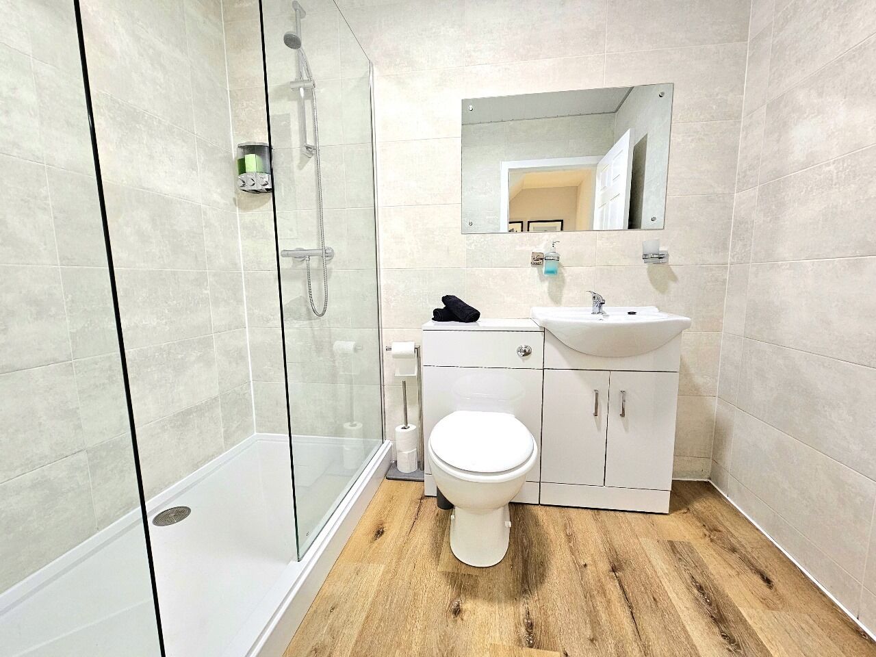 A modern bathroom with a glass shower enclosure, a white toilet, and a sink with a mirror above it.