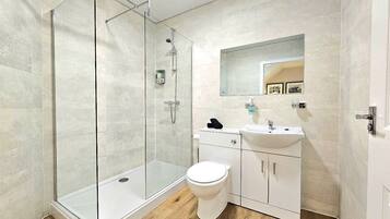 A modern bathroom with a glass-enclosed shower, a white toilet, and a sink with a mirror above it.