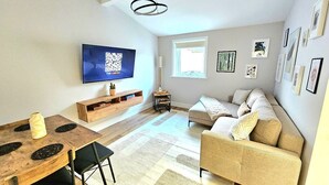 A modern living room with a flat-screen TV, a wooden dining table, a beige sofa, and a small side table. - Warm & Cosy Home in Glasgow (Glasgow)