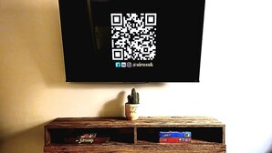 A flat-screen TV mounted on a wall with a QR code below it. - Warm & Cosy Home in Glasgow (Glasgow)