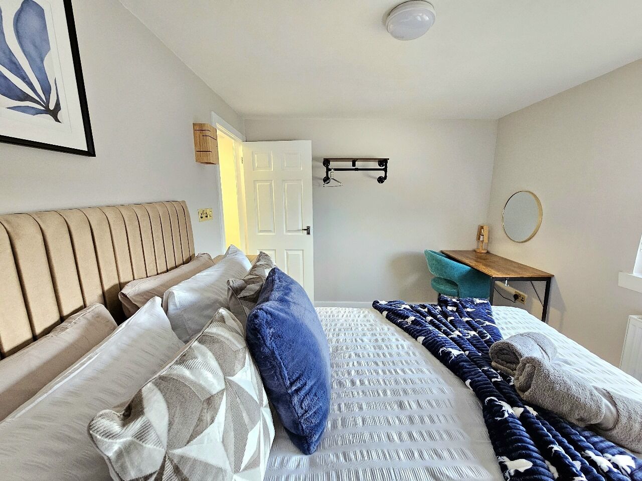 A bedroom with a bed, pillows, a bedside table, a mirror, and a door.