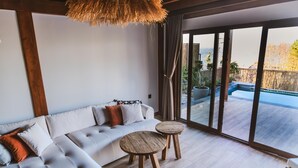 A modern living room with a large sofa, two wooden side tables, and a view of a swimming pool through large glass doors. - Exclusive Hill Sapanca (Sapanca)