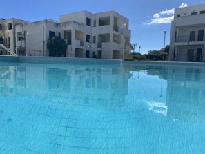 A swimming pool with a tiled surface, surrounded by buildings with balconies and windows.