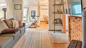 Een woonkamer met een bank, een vloerkleed, een open haard en een eethoek op de achtergrond.