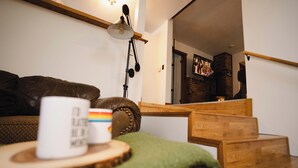 Een gezellige zithoek met een bruine leren bank, een houten bijzettafeltje met een mok, en een trap naar een eetgedeelte.
