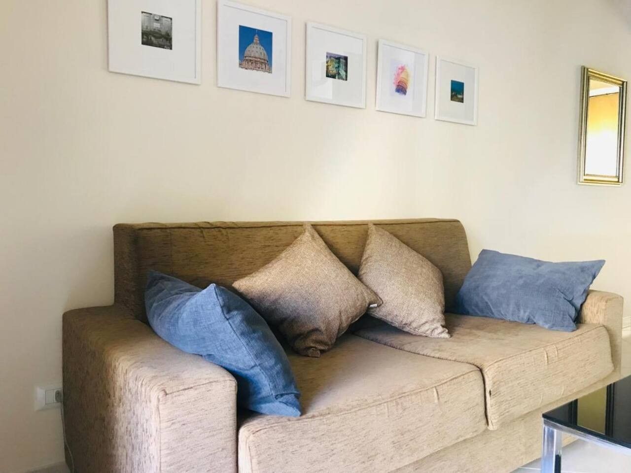 En beige sofa med fire puder, et billede i ramme på væggen og et spejl.