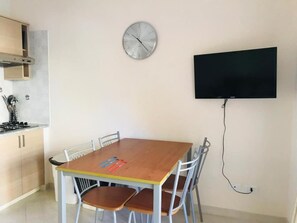 Un coin repas comprenant une table en bois, six chaises, une horloge murale et un téléviseur à écran plat.