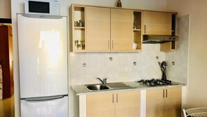 Une cuisine de taille réduite équipée d’un réfrigérateur, d’un évier, d’une cuisinière et de meubles de rangement en bois.