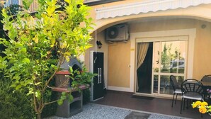 Une terrasse avec un barbecue, une porte et un espace détente avec des chaises.