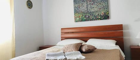 A neatly made bed with a striped bedspread and pillows, a wooden headboard, and a painting on the wall.