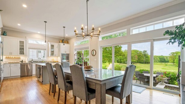 A spacious kitchen with a large dining table, modern appliances, and a view of a lush garden. - Golf-front Personal Arcade Hot tub Outdoor Kitchen (Old Orchard Beach)