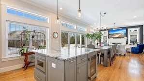 A spacious kitchen with a large island, wooden flooring, and ample natural light from large windows. - Golf-front Personal Arcade Hot tub Outdoor Kitchen (Old Orchard Beach)