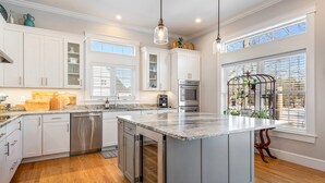A modern kitchen with white cabinetry, stainless steel appliances, and a large island. - Golf-front Personal Arcade Hot tub Outdoor Kitchen (Old Orchard Beach)