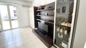 Ein modernes Wohnzimmer mit Flachbildfernseher, eingebauten Regalen und einer Glastürvitrine mit Dekorationsobjekten.