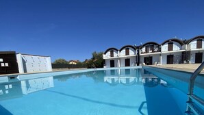 Ein Swimmingpool mit glasklarer, blauer Wasserfläche, umgeben von einem weißen Gebäude mit Balkonen.